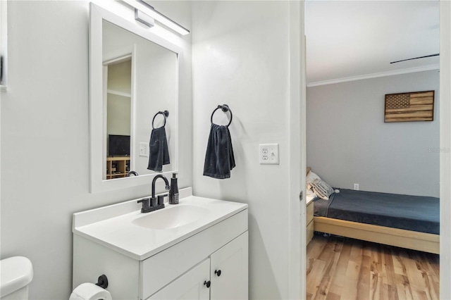 bathroom with toilet, wood finished floors, vanity, and ornamental molding