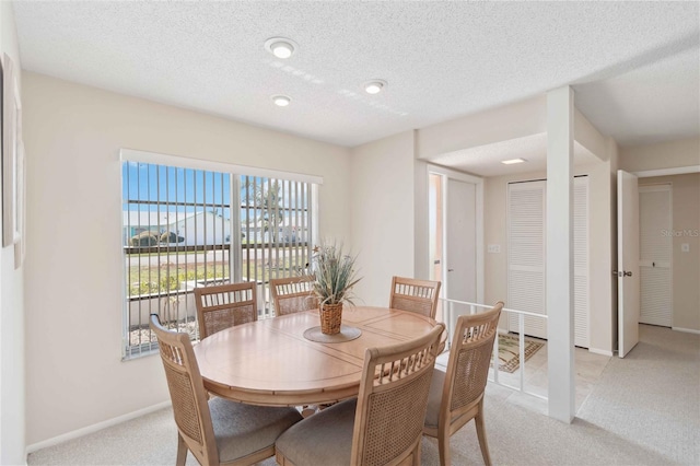 dining area featuring light colored carpet, a textured ceiling, and baseboards