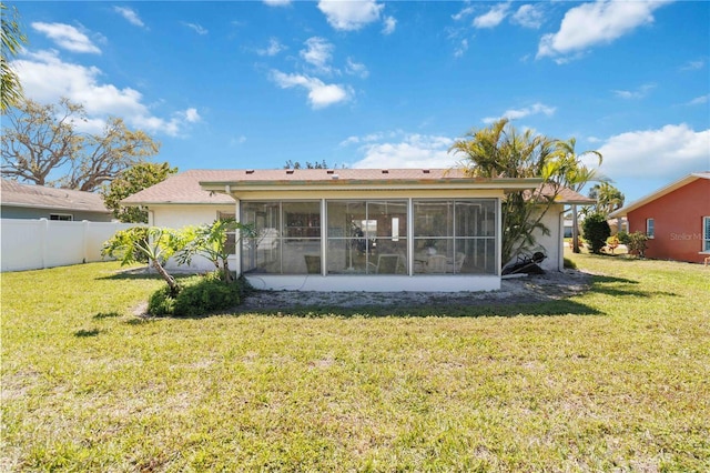 rear view of house with stucco siding, fence, a yard, and a sunroom