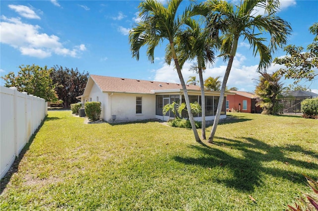 rear view of property featuring stucco siding, a lawn, a sunroom, and fence