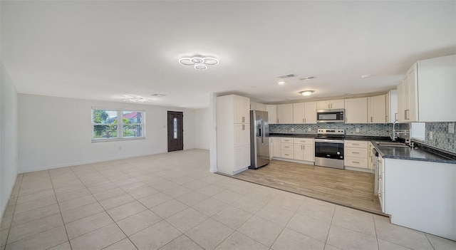 kitchen featuring dark countertops, backsplash, open floor plan, light tile patterned floors, and stainless steel appliances