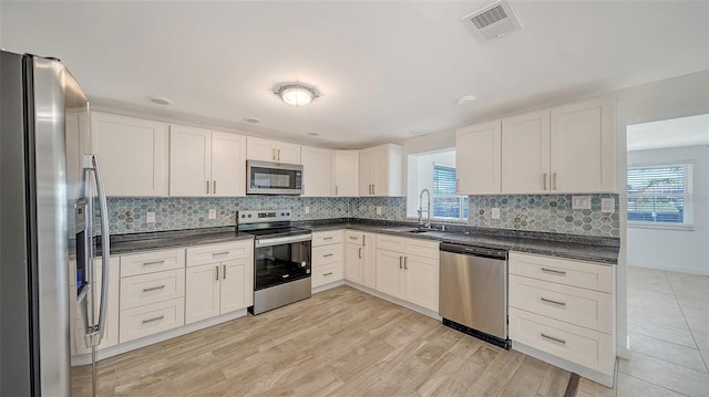 kitchen with a sink, stainless steel appliances, dark countertops, and visible vents