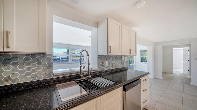 kitchen featuring dishwasher, light tile patterned floors, decorative backsplash, dark stone countertops, and a sink