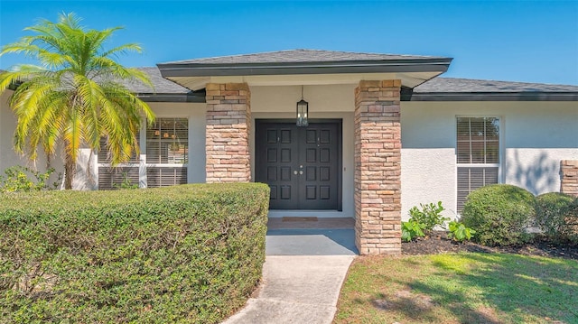 view of exterior entry featuring stone siding, a shingled roof, and stucco siding