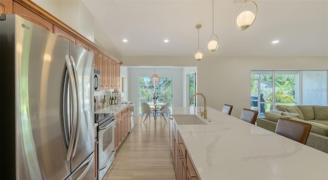 kitchen featuring stainless steel appliances, a sink, open floor plan, light wood-type flooring, and light stone countertops