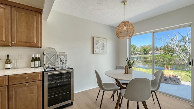 dining room with a textured ceiling, wine cooler, a dry bar, baseboards, and light wood finished floors