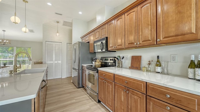 kitchen featuring light wood-style flooring, stainless steel appliances, a sink, visible vents, and brown cabinetry