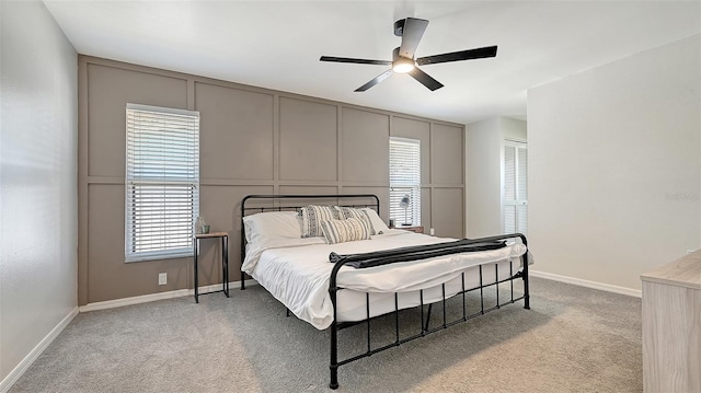 bedroom featuring light carpet, baseboards, a decorative wall, and a ceiling fan