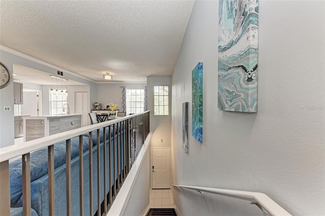 hallway with a textured ceiling, a textured wall, a sink, and an upstairs landing