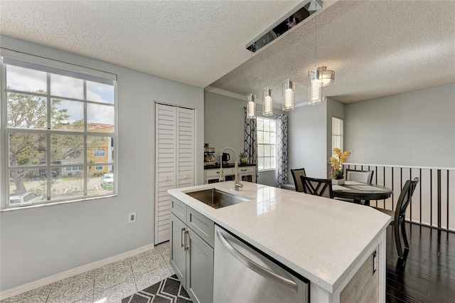 kitchen with baseboards, decorative light fixtures, a kitchen island with sink, stainless steel dishwasher, and a sink