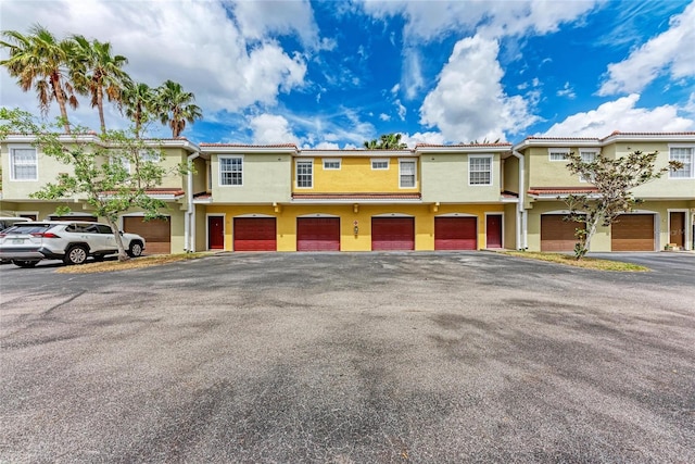 townhome / multi-family property featuring a garage, driveway, a tiled roof, and stucco siding