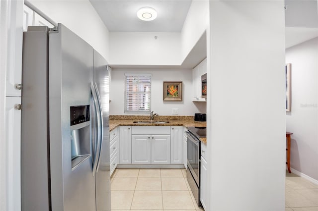 kitchen with appliances with stainless steel finishes, light tile patterned flooring, stone countertops, white cabinetry, and a sink