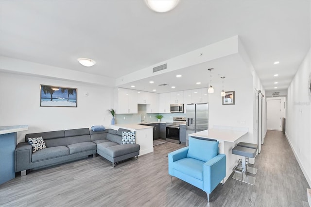 living area with a barn door, recessed lighting, visible vents, baseboards, and light wood-style floors