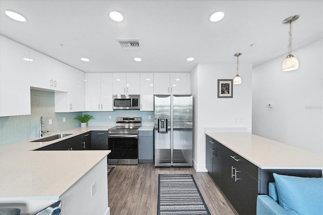 kitchen featuring stainless steel appliances, light countertops, visible vents, a sink, and a peninsula