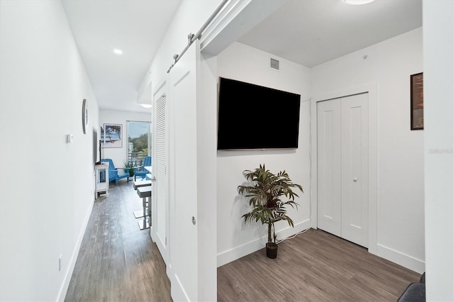 hallway with a barn door, baseboards, wood finished floors, and recessed lighting