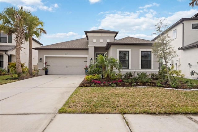 prairie-style home featuring a garage, concrete driveway, roof with shingles, stucco siding, and a front lawn