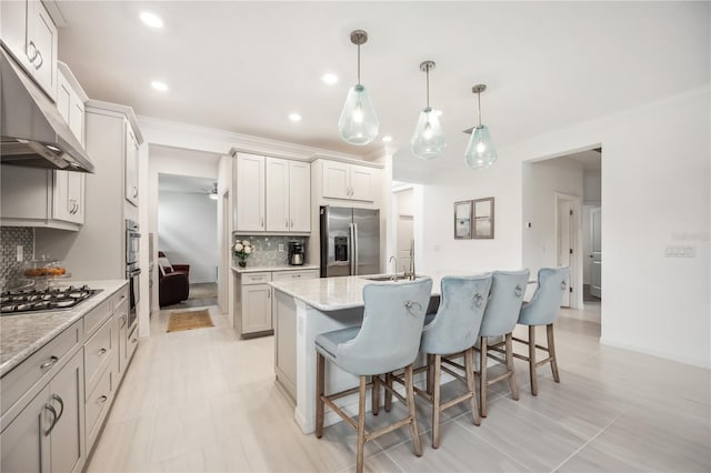 kitchen featuring under cabinet range hood, a breakfast bar, appliances with stainless steel finishes, decorative backsplash, and a center island with sink