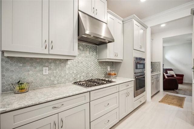 kitchen with appliances with stainless steel finishes, ornamental molding, under cabinet range hood, white cabinetry, and backsplash