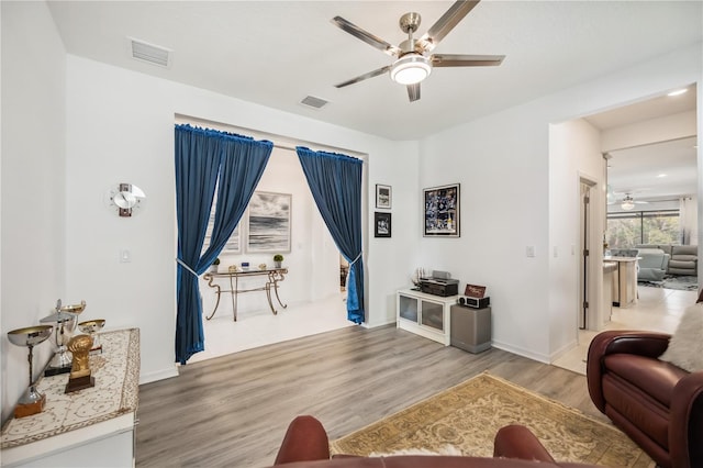 living area with baseboards, wood finished floors, visible vents, and a ceiling fan