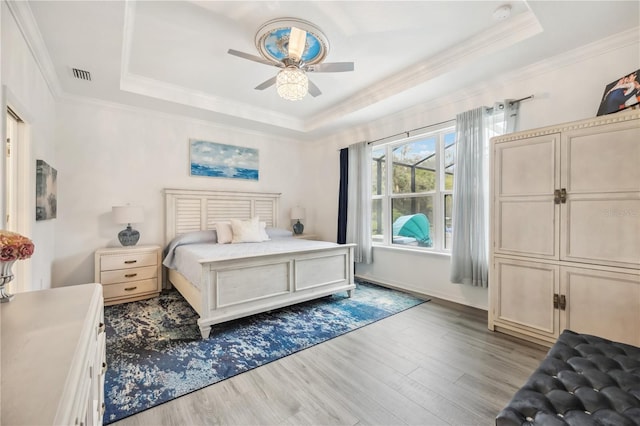 bedroom featuring ornamental molding, a tray ceiling, wood finished floors, and visible vents