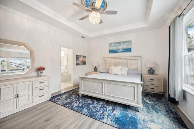 bedroom with a tray ceiling, multiple windows, wood finished floors, and crown molding