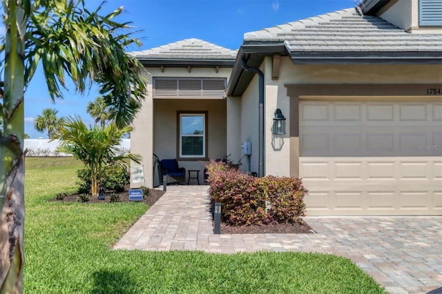 view of exterior entry featuring a garage, a yard, a tiled roof, and stucco siding