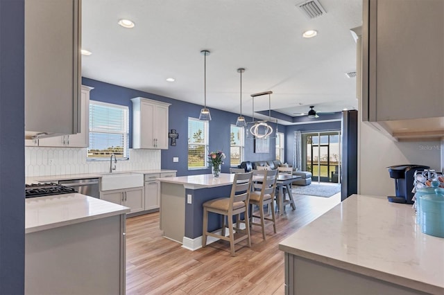 kitchen featuring decorative light fixtures, light wood finished floors, tasteful backsplash, visible vents, and open floor plan