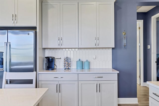 kitchen featuring decorative backsplash, stainless steel refrigerator with ice dispenser, light countertops, and wood finished floors