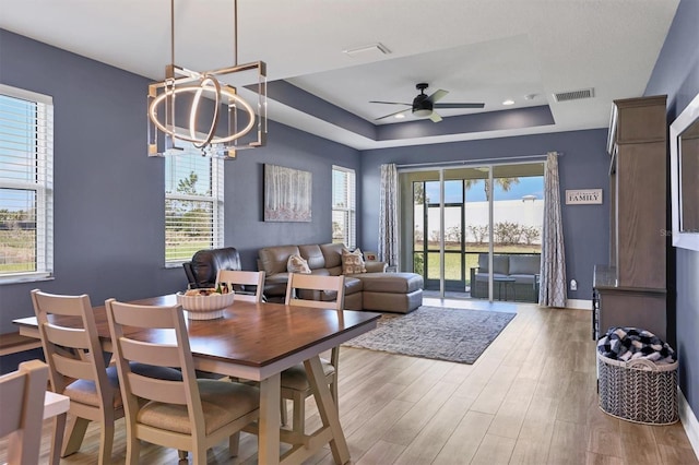 dining room with baseboards, visible vents, wood finished floors, a tray ceiling, and ceiling fan with notable chandelier