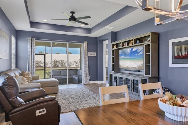 living area featuring baseboards, a raised ceiling, wood finished floors, ceiling fan with notable chandelier, and recessed lighting