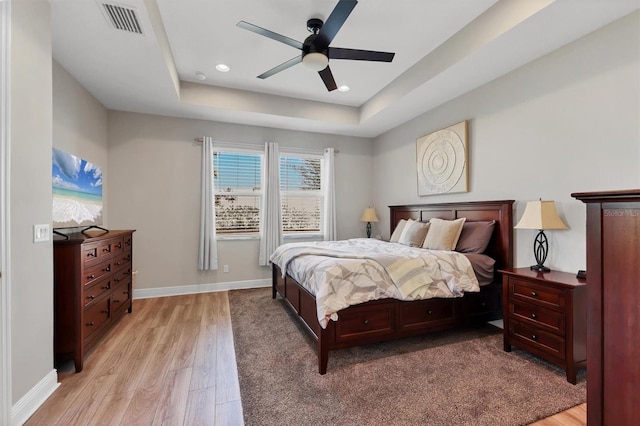 bedroom featuring recessed lighting, visible vents, baseboards, a tray ceiling, and light wood finished floors