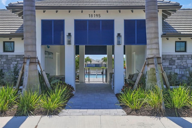 view of exterior entry featuring stone siding, a tile roof, a gate, and stucco siding