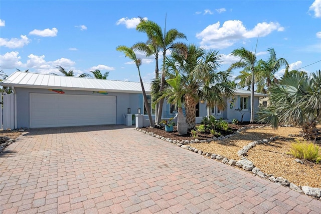 ranch-style home with decorative driveway, metal roof, an attached garage, and stucco siding