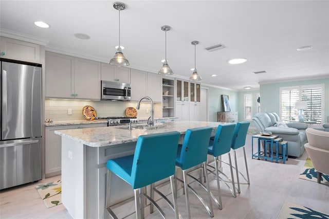 kitchen featuring visible vents, a center island with sink, a sink, appliances with stainless steel finishes, and crown molding