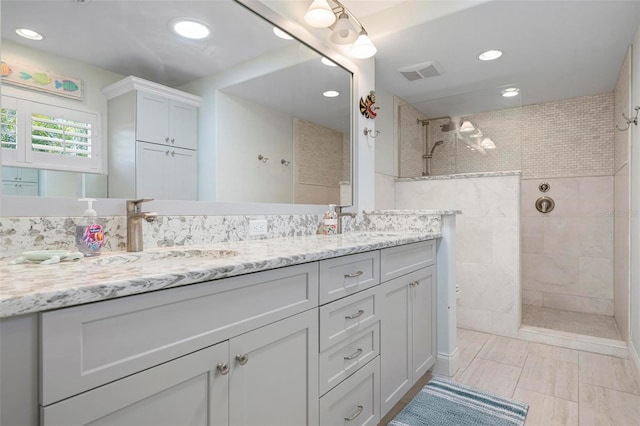 bathroom with double vanity, a walk in shower, visible vents, and a sink