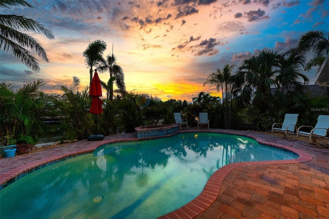 pool at dusk with a patio area, an outdoor pool, and an in ground hot tub