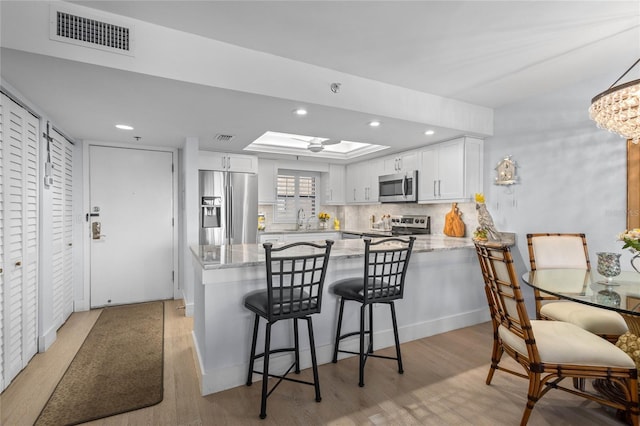 kitchen featuring visible vents, light stone counters, appliances with stainless steel finishes, a peninsula, and white cabinetry