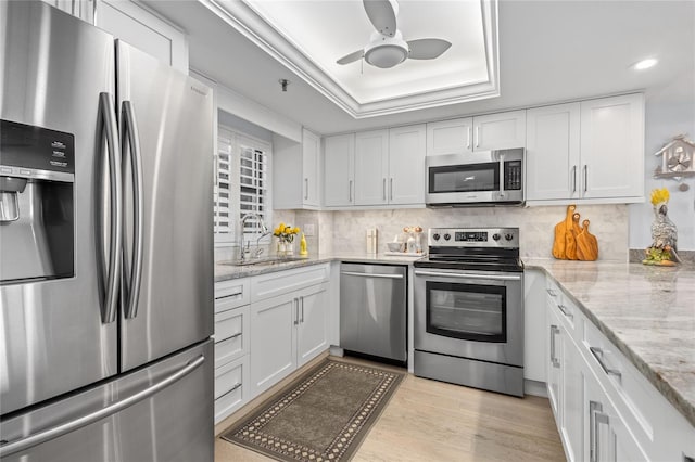 kitchen featuring light wood finished floors, a sink, stainless steel appliances, white cabinetry, and a raised ceiling