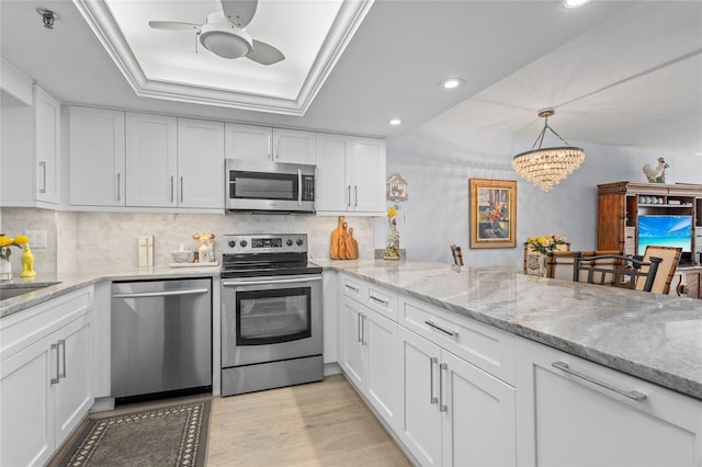 kitchen with a tray ceiling, light wood-style flooring, decorative backsplash, appliances with stainless steel finishes, and white cabinetry