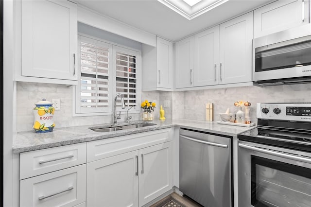 kitchen with backsplash, light stone counters, appliances with stainless steel finishes, white cabinets, and a sink