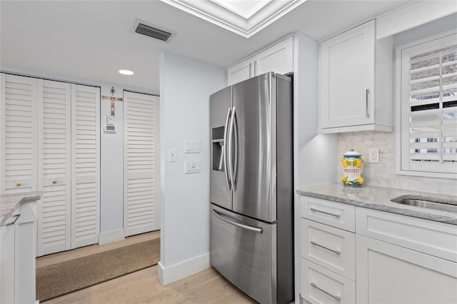 kitchen with light stone counters, visible vents, white cabinetry, and stainless steel refrigerator with ice dispenser