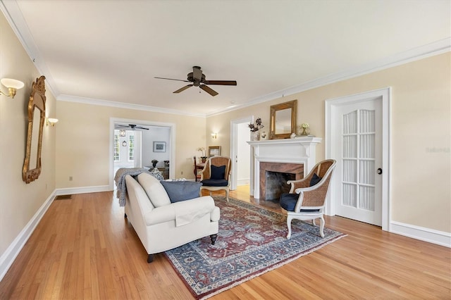 living area with crown molding, a fireplace, light wood-style floors, ceiling fan, and baseboards