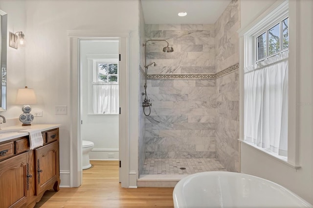 full bath with tiled shower, wood finished floors, vanity, a freestanding tub, and a wealth of natural light