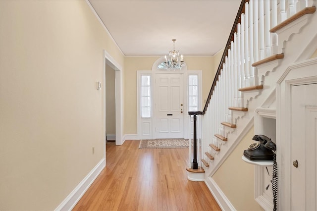 entryway featuring light wood finished floors, stairway, an inviting chandelier, ornamental molding, and baseboards