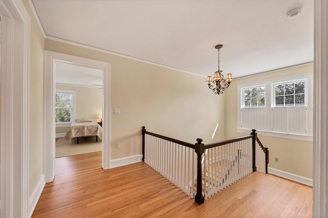 hall featuring light wood-type flooring, baseboards, crown molding, and an upstairs landing