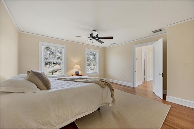 bedroom featuring visible vents, baseboards, a ceiling fan, wood finished floors, and crown molding