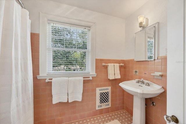 full bath with a wainscoted wall, curtained shower, a sink, and tile walls