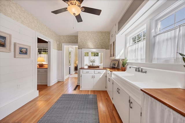 kitchen with wallpapered walls, white cabinetry, light wood finished floors, and a sink