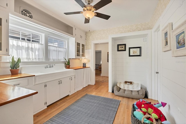 kitchen featuring white cabinets, light countertops, light wood finished floors, glass insert cabinets, and wallpapered walls