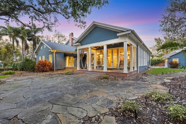 back of property at dusk with french doors, a chimney, and a porch